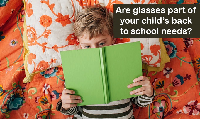 young blonde haired boy laying on colorful pillow and couch reads book holding it close to face as if he might need glasses